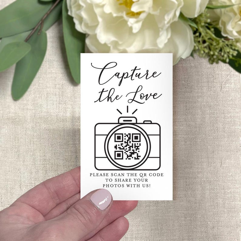 May include: A white card with the text "Capture the Love" in elegant script, featuring a camera graphic with a QR code. The card also includes the text "PLEASE SCAN THE QR CODE TO SHARE YOUR PHOTOS WITH US!"