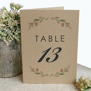 Op de afbeelding: Een bruine kaart met een bloemmotief en de tekst "TABLE 13" in zwart.