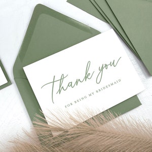 May include: A white card with green calligraphy that says "Thank you for being my bridesmaid". The card is in a sage green envelope.
