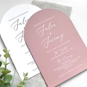 May include: Two wedding invitations with a pink and white arch design. The text on the white invitation reads "Welcome to the wedding of Julia and Jeremy." The text on the pink invitation reads "Welcome to the wedding of Julia and Jeremy." The pink invitation also includes the date and time of the wedding, the location, and the ceremony details.