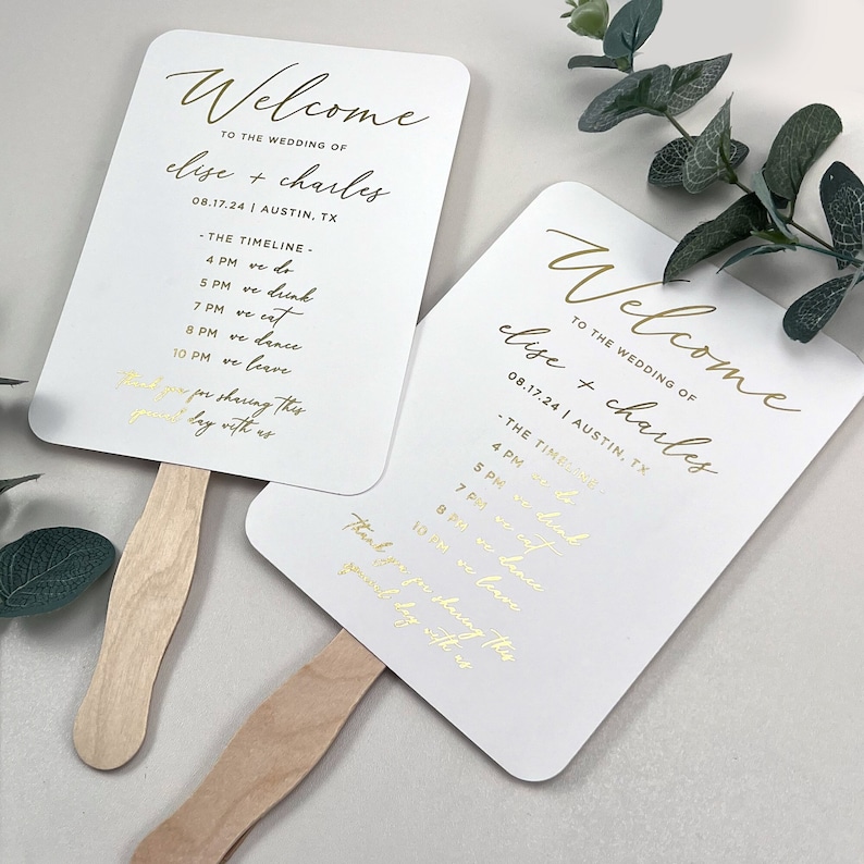 May include: White wedding fan with gold lettering. The fan says "Welcome to the wedding of Elise + Charles 08.17.24 | Austin, TX" and includes a timeline of events for the wedding day.