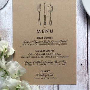 Op de afbeelding: Een bruine papieren menukaart met een vintage bestekillustratie en een lijst met gerechten voor een huwelijksreceptie. Het menu bevat Zomersalade met biologische babygroenten, Gebakken Wilde Zalm, Angus Certified Boneless Short Ribs, Trouwtaart en koffie- en theeservice.