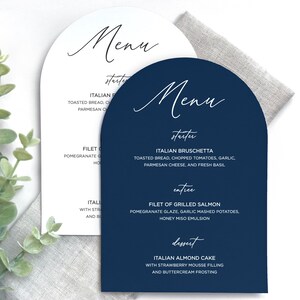 May include: Two arched menu cards, one white and one navy blue, featuring elegant script headings for Menu, starter, entree, and dessert. The text lists Italian Bruschetta, Filet of Grilled Salmon, and Italian Almond Cake with detailed descriptions.