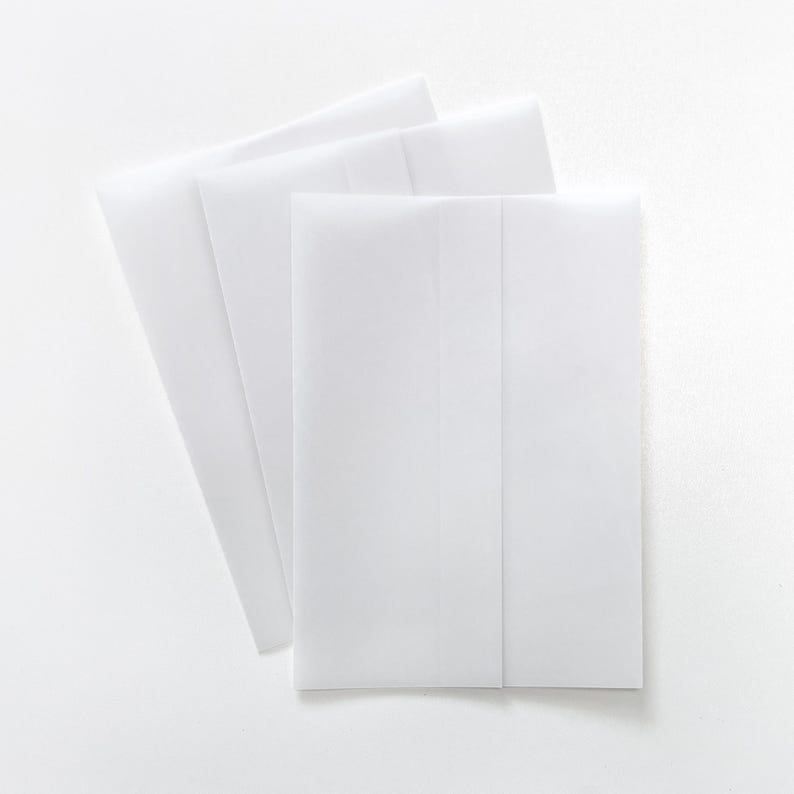 May include: A collection of white paper envelopes arranged on a white surface. The envelopes are rectangular with a folded flap, and are slightly translucent. The image is a top-down view, with the envelopes overlapping each other.
