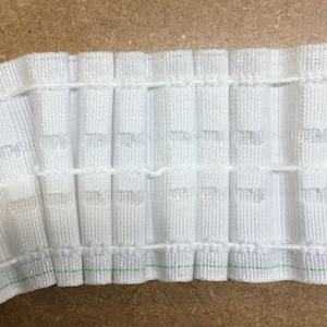 May include: White pleated curtain tape with a green thread running along the bottom edge. The tape is designed to create pleats in curtains.
