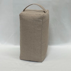Può includere: Un fermaporta rettangolare in tessuto beige, con una piccola maniglia arcuata sulla parte superiore. Il fermaporta è realizzato in un materiale strutturato ed è progettato per impedire la chiusura delle porte. Il colore neutro si adatta a vari stili di arredamento.