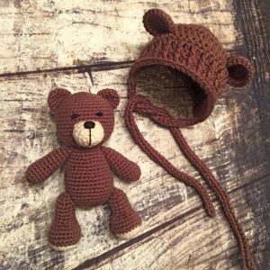 Puede incluir: Un oso de peluche de crochet marr&oacute;n con ojos negros y un gorro de crochet marr&oacute;n con orejeras.