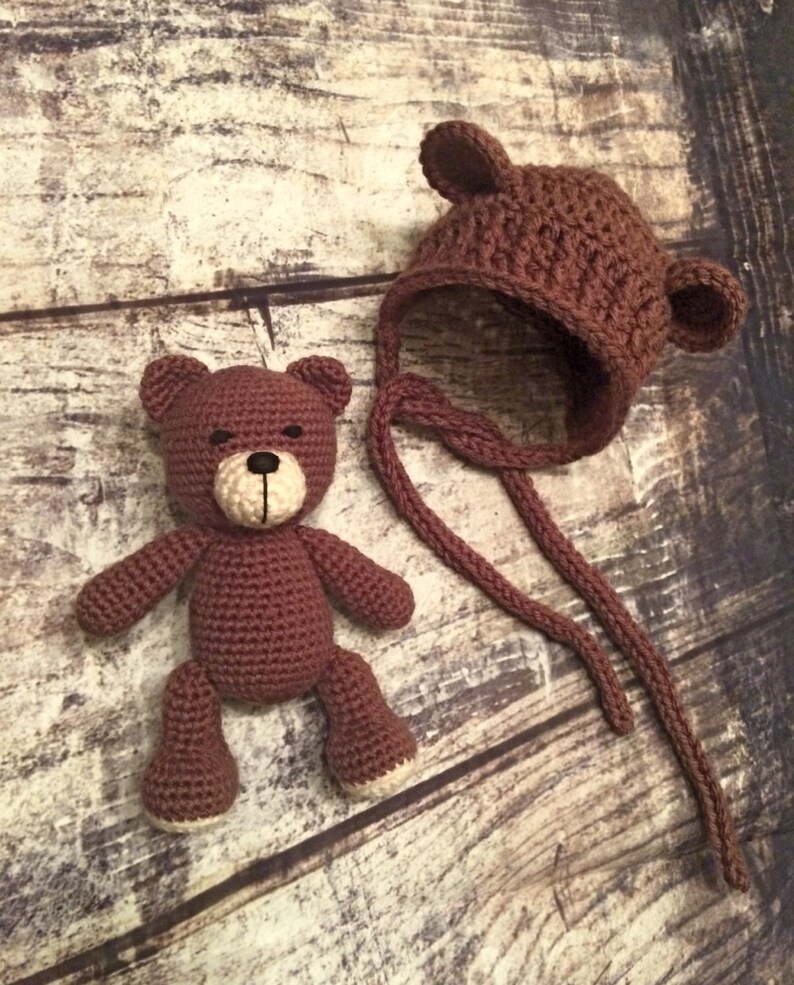 Puede incluir: Un oso de peluche de crochet marr&oacute;n con ojos negros y un gorro de crochet marr&oacute;n con orejeras.