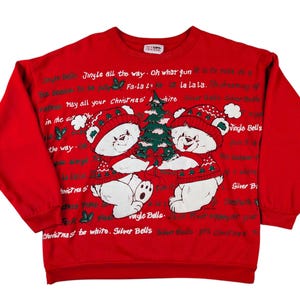 Könnte beinhalten: Roter Weihnachts-Sweatshirt mit zwei weißen Bären, die Hüte und Pullover tragen und einen grünen Weihnachtsbaum halten. Der Pullover hat den Text "Jingle Bells" und "Silver Bells". Ein festlicher Weihnachts-Pullover.