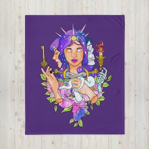 May include: A purple throw blanket featuring a mystical illustration. The artwork depicts a woman with a celestial headpiece, a key, a snake, and a skull. The design includes floral elements and a candle.