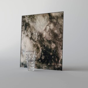 May include: A stack of four clear glass shot glasses in front of a square piece of glass with a dark brown and black mottled pattern.
