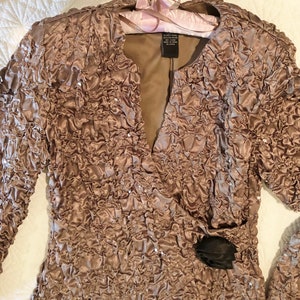 May include: A brown sequined jacket with a ruffled texture and a black flower accent. The jacket has a V-neck and long sleeves.