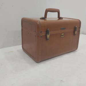 May include: A vintage brown suitcase with a top handle, brass-coloured latches, and a keyhole. The rectangular case has rounded corners and a stitched design. A classic travel accessory.