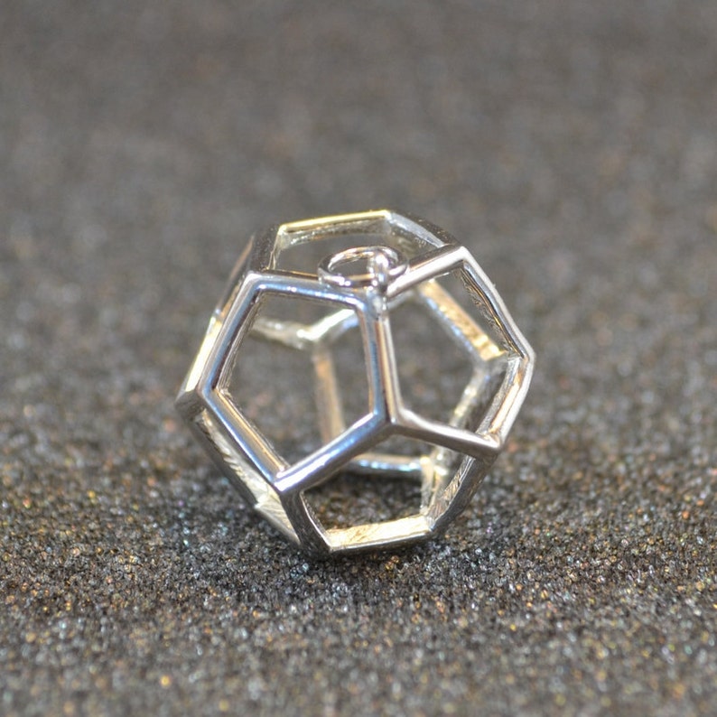 Peut inclure: Un pendentif g&eacute;om&eacute;trique en argent avec une boucle en haut pour attacher une cha&icirc;ne. Le pendentif est une forme creuse tridimensionnelle &agrave; multiples facettes.