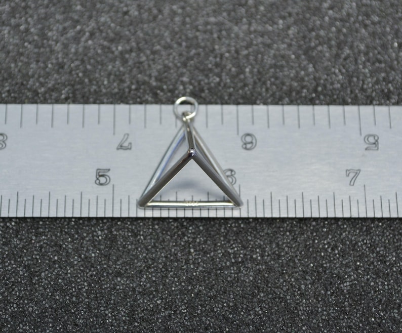 Puede incluir: Un amuleto de plata con forma de tri&aacute;ngulo tridimensional.