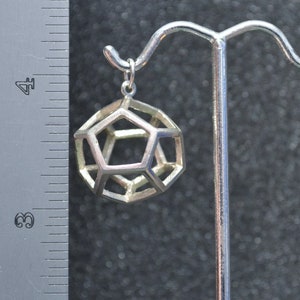Peut inclure: Un pendentif g&eacute;om&eacute;trique argent&eacute; en forme de dod&eacute;ca&egrave;dre, suspendu &agrave; un crochet argent&eacute;.