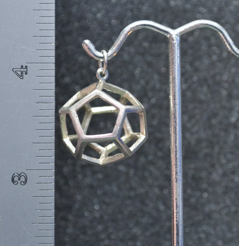Peut inclure: Un pendentif g&eacute;om&eacute;trique argent&eacute; en forme de dod&eacute;ca&egrave;dre, suspendu &agrave; un crochet argent&eacute;.