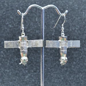 Puede incluir: Un par de pendientes de plata con forma de estación espacial con paneles solares. Los pendientes están colgados de un soporte de plata.