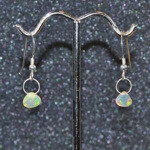 May include: A pair of silver earrings with teardrop-shaped opal stones. The opals have a white base with iridescent green, blue, and yellow flashes.