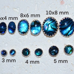 May include: Assortment of abalone shell cabochons in various sizes, ranging from 3 mm to 10 mm. The cabochons are set in silver bezels with a scalloped edge. The abalone shell has a blue, green, and purple iridescent sheen.