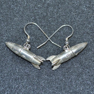 May include: A pair of silver rocket ship earrings. The earrings are made of metal and have a detailed design.