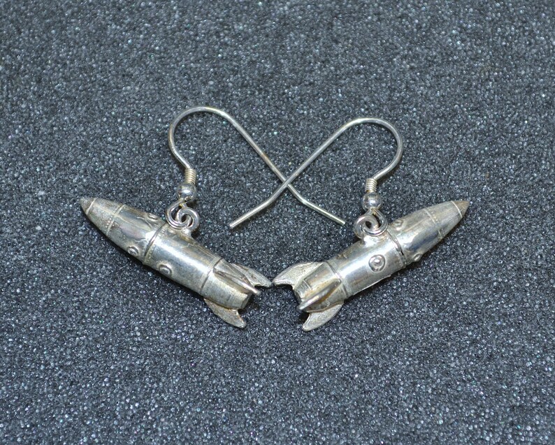 May include: A pair of silver rocket ship earrings. The earrings are made of metal and have a detailed design.