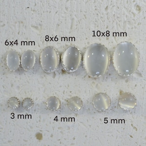 May include: A set of white oval cabochon gemstone earrings in various sizes, ranging from 3 mm to 10 mm. The earrings are set in silver and have a scalloped edge.