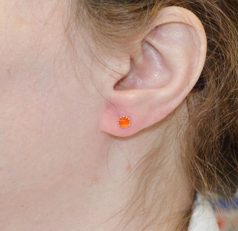 May include: A close-up of a person's ear with a small orange stud earring.