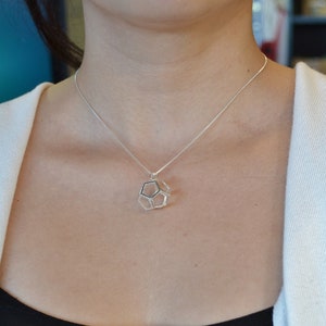 Peut inclure: Un collier en argent avec un pendentif g&eacute;om&eacute;trique. Le pendentif est une forme tridimensionnelle avec un centre creux.