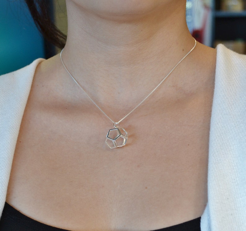 Peut inclure: Un collier en argent avec un pendentif g&eacute;om&eacute;trique. Le pendentif est une forme tridimensionnelle avec un centre creux.