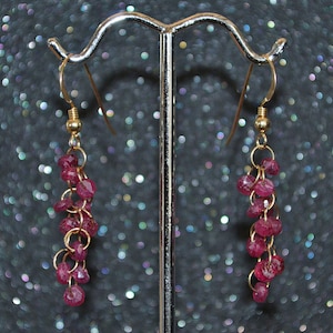 May include: A pair of dangle earrings with a gold chain and pink ruby stones.
