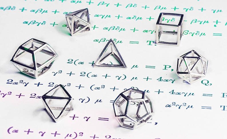 Puede incluir: Una colecci&oacute;n de seis formas geom&eacute;tricas plateadas, incluyendo un cubo, una pir&aacute;mide y un dodecaedro, est&aacute;n dispuestas sobre una superficie blanca con ecuaciones matem&aacute;ticas escritas a mano en tinta verde.