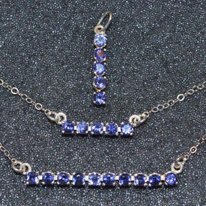 May include: A set of three silver necklaces with blue gemstone accents. The necklaces feature a variety of lengths and styles, including a pendant necklace with a vertical row of gemstones and two bar necklaces with horizontal rows of gemstones.