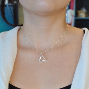 Puede incluir: Un collar de cadena de plata con un colgante de tri&aacute;ngulo geom&eacute;trico.