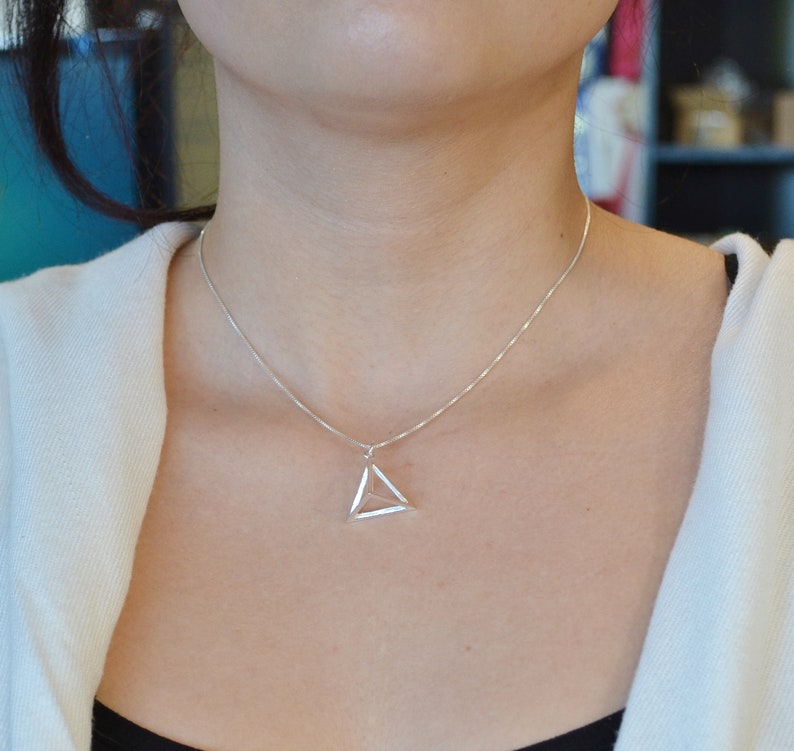 Puede incluir: Un collar de cadena de plata con un colgante de tri&aacute;ngulo geom&eacute;trico.