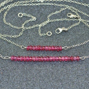 May include: Two delicate silver chains with a pink gemstone bead necklace. The necklace is made of small, round pink beads and is strung on a silver chain. The chains are layered and have a lobster clasp closure.