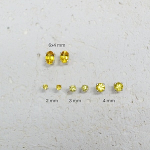 May include: A collection of yellow gemstone earrings in various sizes. The earrings include oval-cut 6x4 mm stones, and round-cut stones in 2 mm, 3 mm, and 4 mm sizes. The earrings are set against a neutral background.