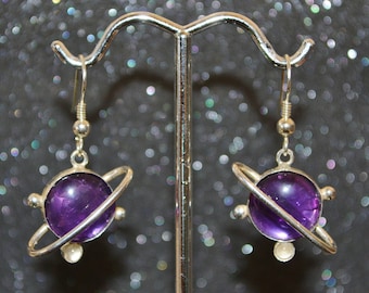 Puede incluir: Un par de pendientes de plata con piedras preciosas de amatista engastadas en un diseño de anillo, que se asemejan a un planeta con un sistema de anillos.