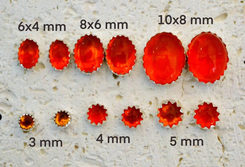 May include: Assortment of orange glass cabochons in various sizes, ranging from 3 mm to 10x8 mm. The cabochons are set in silver bezels with a scalloped edge.