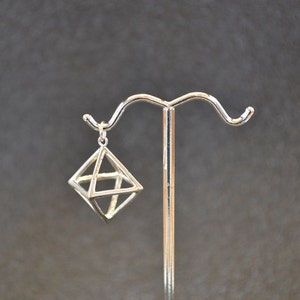 May include: A silver geometric pendant in the shape of a cube with a triangular opening on each side. The pendant is hanging from a silver stand.