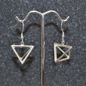 May include: A pair of silver geometric triangle earrings hanging from a silver stand. The earrings are made of two triangles that intersect each other.