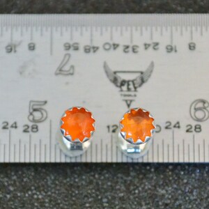 May include: A pair of orange gemstone cufflinks with a silver setting. The cufflinks are measured against a ruler.
