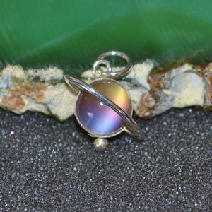 May include: A silver charm with a iridescent glass sphere surrounded by a silver ring, resembling a planet in orbit.