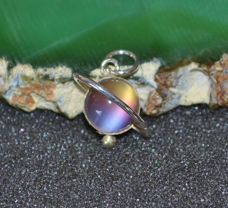 May include: A silver charm with a iridescent glass sphere surrounded by a silver ring, resembling a planet in orbit.