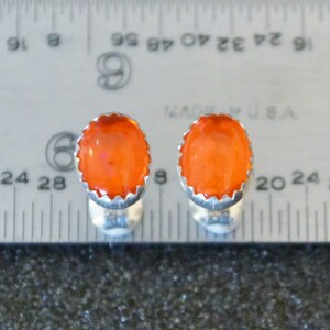 May include: A pair of silver cufflinks with orange gemstone cabochons. The cufflinks are set against a ruler for size reference.
