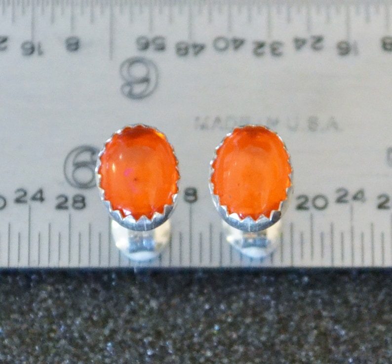 May include: A pair of silver cufflinks with orange gemstone cabochons. The cufflinks are set against a ruler for size reference.