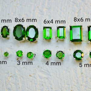 Puede incluir: Un conjunto de pendientes de piedras preciosas verdes de diferentes tamaños, que van desde los 2 mm hasta los 8 mm. Los pendientes se muestran sobre una superficie blanca texturizada. El texto "6x4 mm", "8x6 mm", "2 mm", "3 mm", "4 mm" y "5 mm" está impreso debajo de cada par de pendientes.