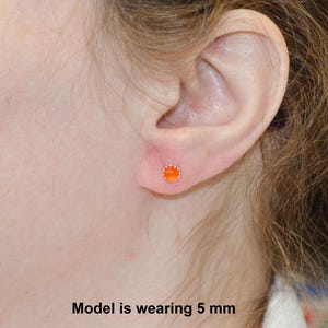 May include: A close-up of a person's ear with a small orange stud earring. The model is wearing a 5 mm earring.