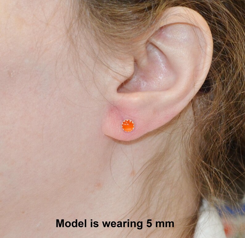 May include: A close-up of a person's ear with a small orange stud earring. The model is wearing a 5 mm earring.