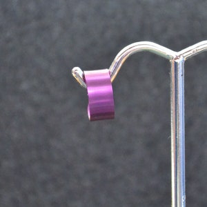 Puede incluir: Un anillo de metal morado en un soporte de exhibición. El anillo es liso y brillante.